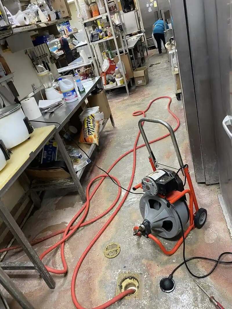 Drain machine and cable clearing a floor drain in a commercial kitchen