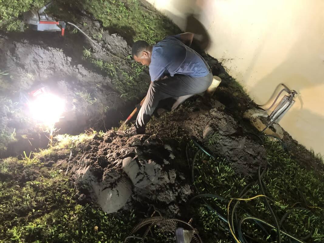 Drain Masters technician digging along a home's foundation at night under a work light