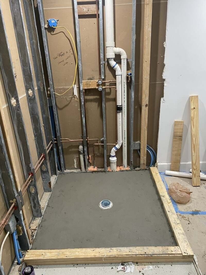 Shower pan and drain roughed in on a concrete slab with the wall plumbing exposed