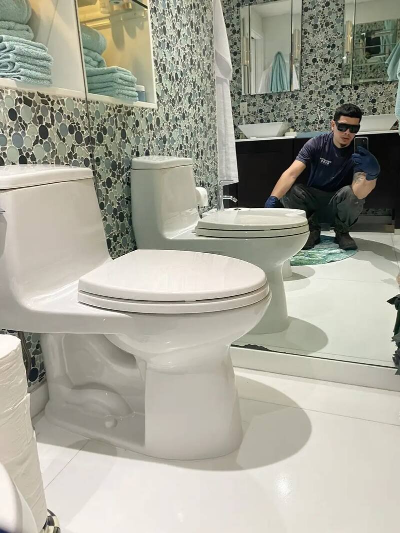 Drain Masters technician setting a new toilet in a tiled bathroom