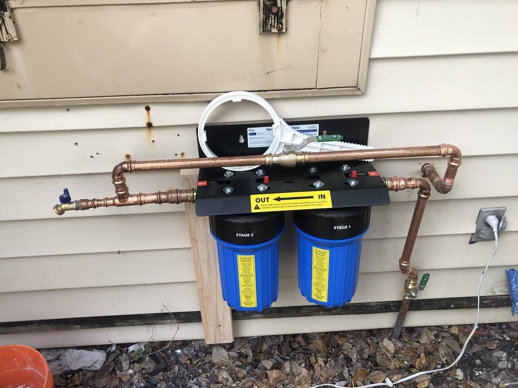 Whole-house two-stage water filter plumbed in copper on an exterior wall