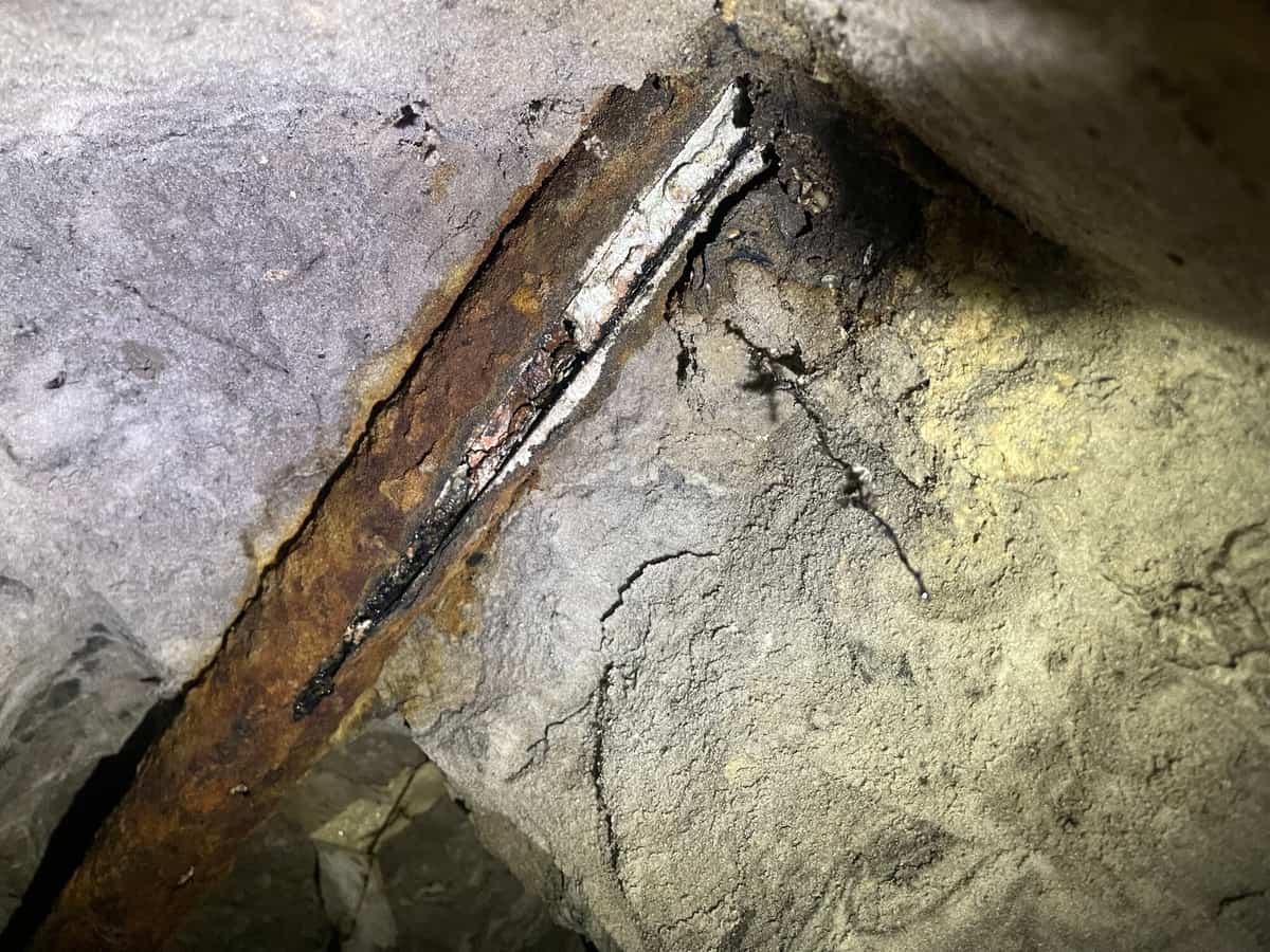Corroded, split cast iron drain pipe exposed under a concrete slab