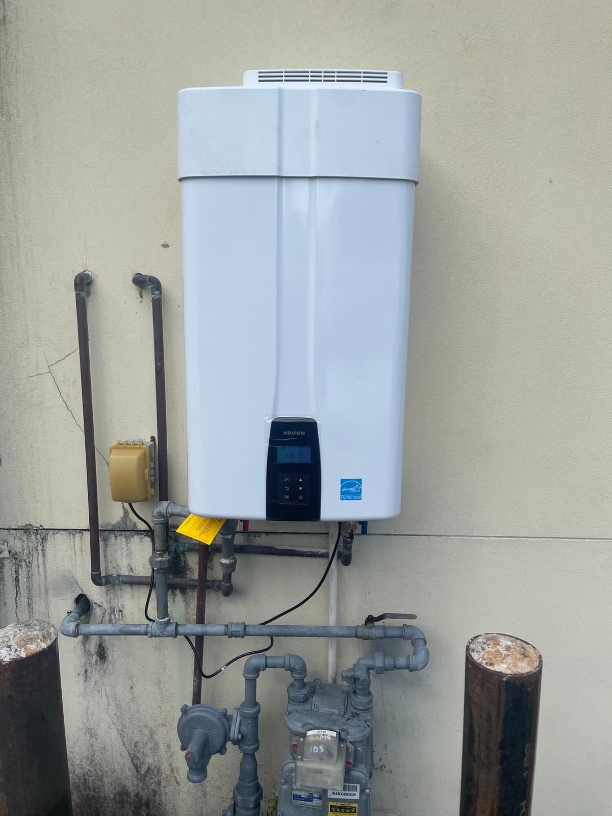 Tankless gas water heater on an exterior wall with its gas piping and meter below